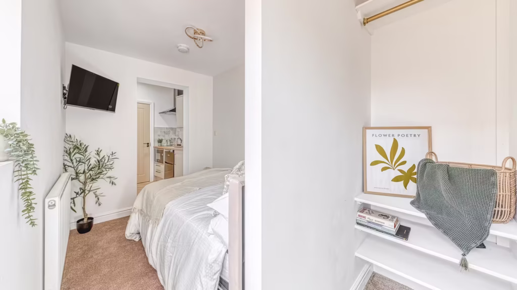 Cozy bedroom with TV, plant, and kitchen access.