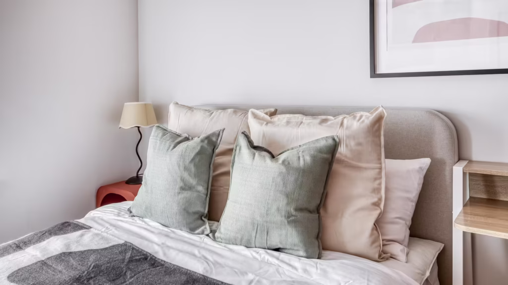 Cosy bed with pastel pillows and a lamp.